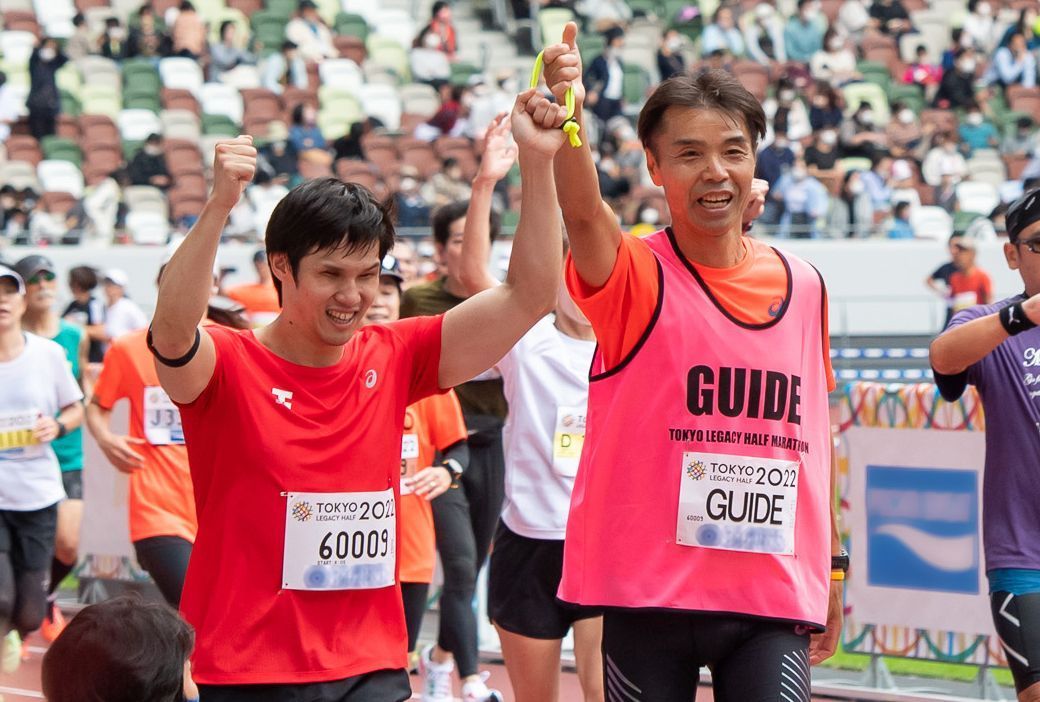 「東京レガシーハーフマラソン2022」の観衆を背にした木村敬一選手と伴走を務めたアシックス社員福成さんの写真